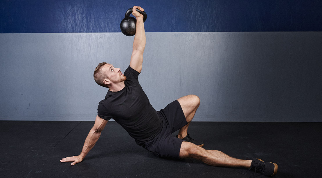 Man performing the turkish get-up exercise using a kettlebell